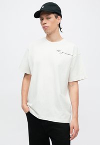 Biała bawełniana koszulka z krótkim rękawem i luźnym krojem, z nadrukowanym tekstem na przodzie. W zestawie czarna czapka i czarne spodnie.