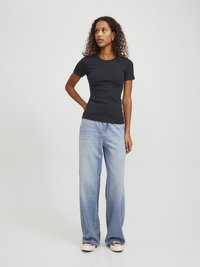 Sort svart tettsittende t-skjorte med rund hals, kombinert med lyseblå vide jeans og hvite sneakers med detaljer.