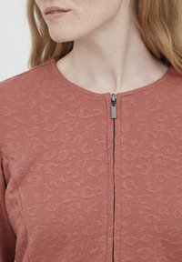 Dulko rožinė zip-up palaidinė su tekstūruotu leopardų raštu, turinti apvalų iškirpimą ir metalinį užtrauktuką priekyje.