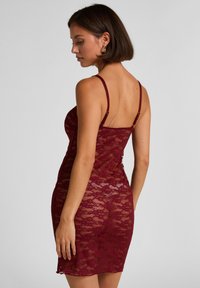 Φόρεμα από μπορντό δαντέλα με λεπτές τιράντες, εφαρμοστό σχέδιο, κυματιστό τελείωμα και διαφανή υφή, που παρουσιάζει ένα λουλουδάτο μοτίβο δαντέλας.