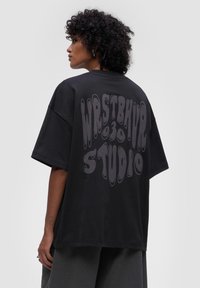 Czarna, oversize koszulka z bawełny z falistym, płynnym wzorem w szarości na plecach. Krótkie rękawy i okrągły dekolt.