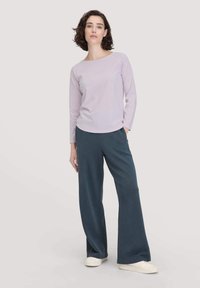 Helles lila Langarmoberteil mit rundem Halsausschnitt, kombiniert mit weit geschnittenen, dunkelblauen Hosen. Glatter Stoff, lockere Passform und weiße Sneakers.