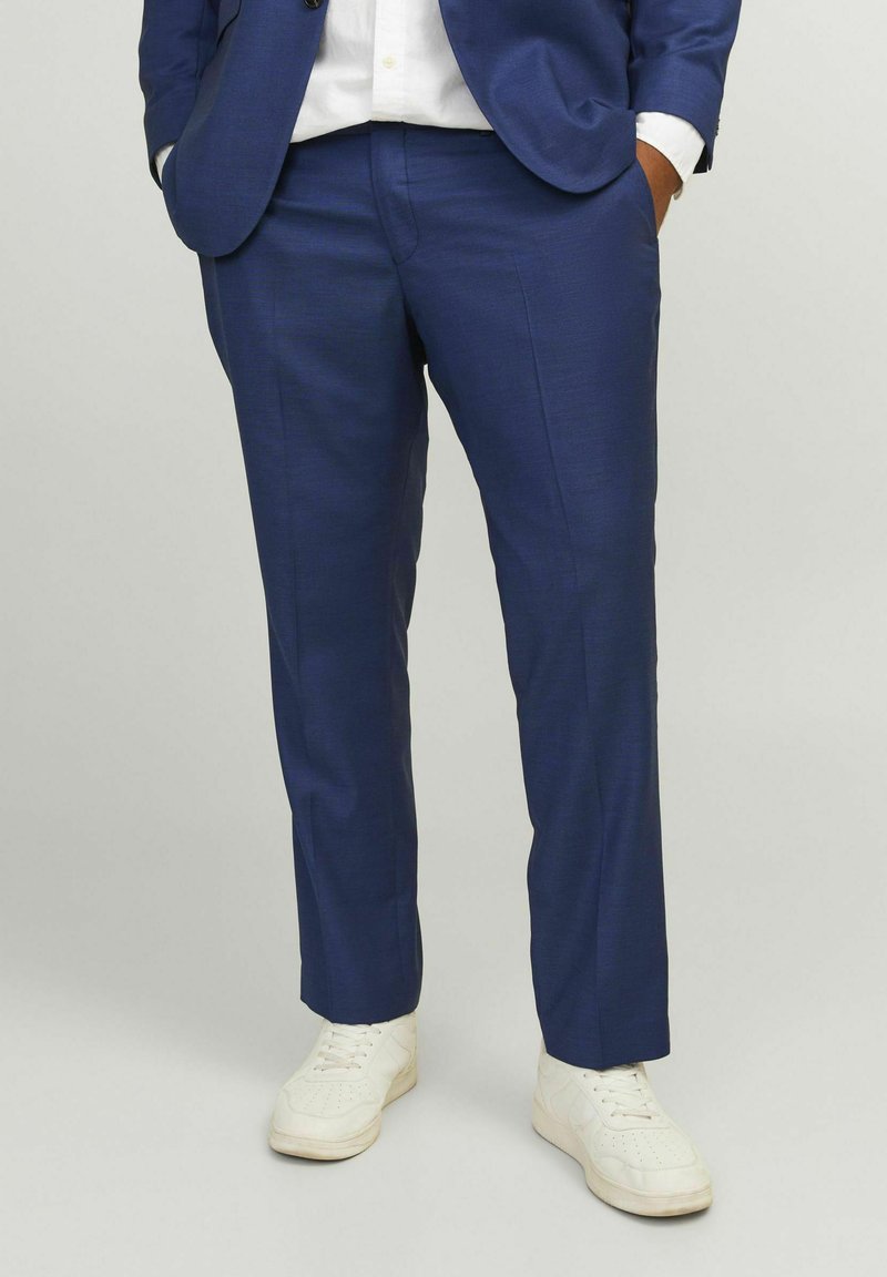 Marineblaue Anzughose aus strukturiertem Stoff, taillierte Passform, mit flachem Bund und Taschen, kombiniert mit weißen Sneakers für einen Kontrast.