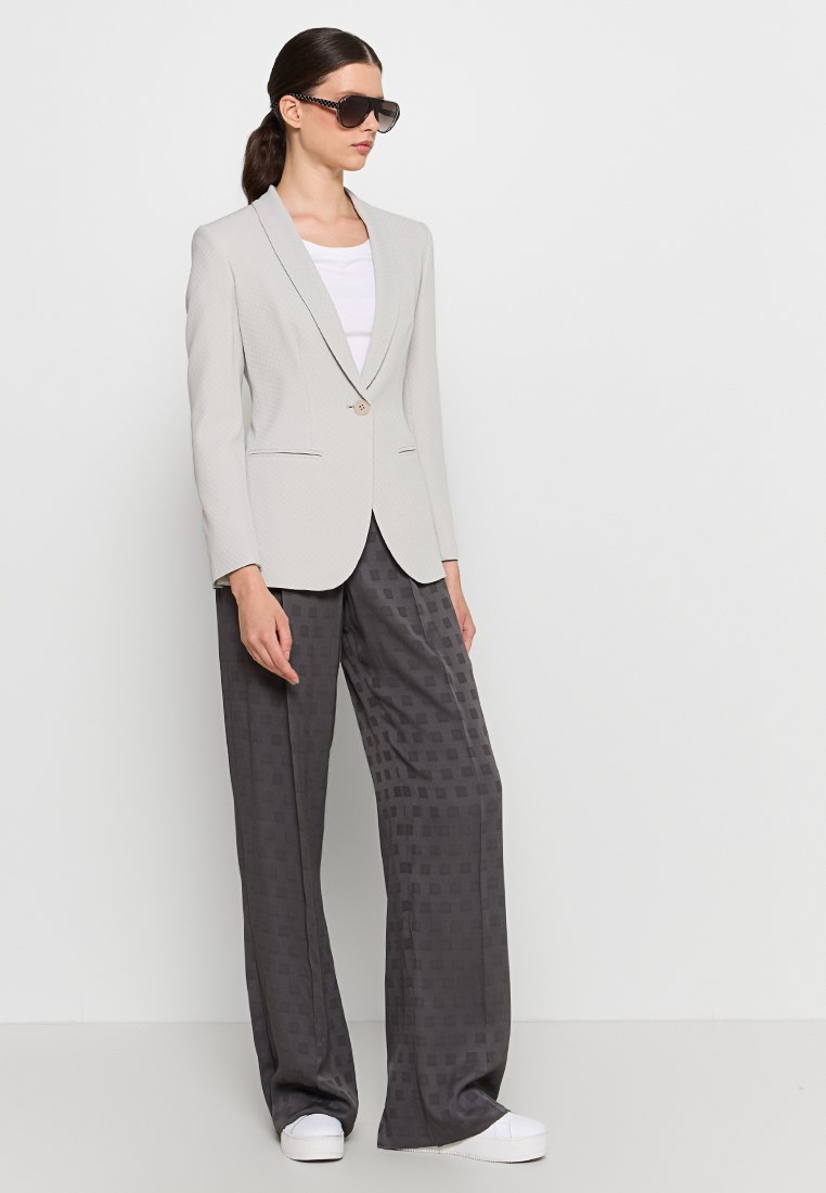 Helles graues Blazer mit einer subtilen gemusterten Textur, Ein-Knopf-Verschluss, kombiniert mit dunkelgrauen weiten Hosen mit einem Quadratmuster.