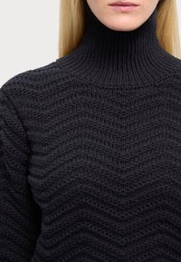Pull en maille gris foncé avec un col haut, présentant un motif en zigzag texturé, fabriqué avec un fil épais et doux.