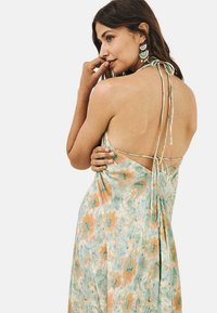 Vestido maxi de tejido ligero y fluido con un estampado floral en tonos pastel, que cuenta con un cierre de lazo en la espalda y un diseño de espalda descubierta.