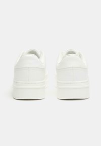 Sneakers bianchi in pelle con una texture liscia, tacco arrotondato e suola leggermente rialzata. Design minimalista senza accenti aggiuntivi.
