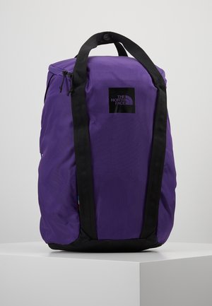 Sac à dos North Face violet avec des poignées noires et un logo à l'avant, présenté sur une surface blanche sur fond neutre.