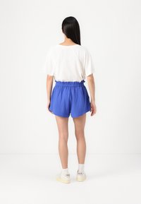 Blå shorts med en samlet elastisk midje, kombinert med en løs hvit topp. Shortsene har et teksturert stoff og en avslappet passform.