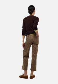 Pull marron avec des bordures jaunes, pantalon imprimé léopard et chaussures marron. La tenue présente une coupe décontractée, des manches de longueur moyenne et un pantalon court.