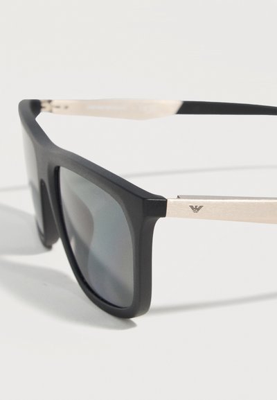 Μαύρα ορθογώνια γυαλιά ηλίου με σκούρους φακούς και ασημένιους μεταλλικούς βραχίονες με μικρό λογότυπο της μάρκας στο πλάι.