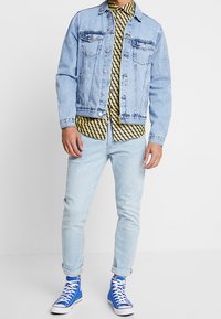 Světle modrá denimová bunda přes žluté a černé pruhované tričko, v kombinaci se světle modrými skinny džíny a modrými vysokými sneaker.