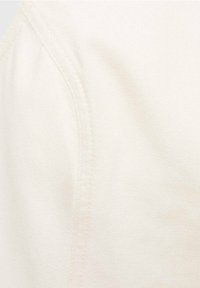 Tissu texturé de couleur crème avec des coutures visibles. Gros plan sur un vêtement montrant une surface lisse et une sensation douce.