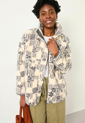 Fleece jacket in cream with gray geometric and floral patterns, zip closure, high collar, and side pockets, worn over a white top.