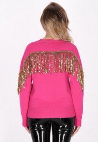Roze trui met gouden pailletten franjes aan de achterkant. Zachte textuur met een geribde zoom en manchetten, gemaakt van een lichte stof.