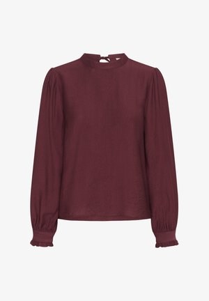 Blusa lunga color marsala con collo alto, chiusura a bottoni sul retro e maniche a sbuffo arricciate con polsini volant. Tessuto liscio.