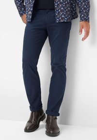 Marineblaue Hose mit geradem Schnitt, aus glattem Material, mit hochgerollten Säumen, kombiniert mit dunkelbraunen Leder-Stiefeletten.