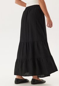 Zwarte gelaagde maxi rok van lichtgewicht stof met een elastische tailleband, met een vloeiende uitstraling en een zachte textuur.