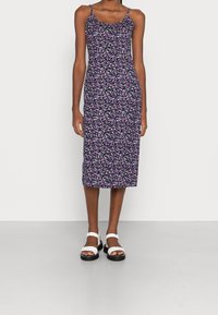 Květinové midi šaty v námořnické modři, s tenkými ramínky a zvýrazněným siluetou. Design obsahuje malé růžové a bílé květinové vzory. Černé platformové sandály.