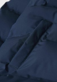 Mørkeblå boblejakke med teksturert overflate og synlig horisontal lomme med søm i matchende tråd.