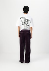 Vit bomullströja med en svart grafik på baksidan, tillsammans med lila sammetsbyxor med elastisk midja och sidofickor.