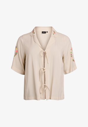 Blouse beige à manches courtes avec col, broderie décorative sur les manches et fermeture à nouer à l'avant. Texture du tissu lisse.