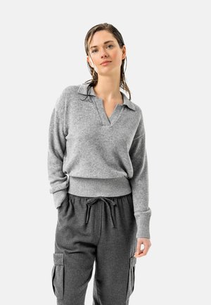 Grauer Pullover mit V-Ausschnitt und geripptem Saum, kombiniert mit dunkelgrauen Cargo-Hosen mit Kordelzug. Das Material wirkt weich und strukturiert.