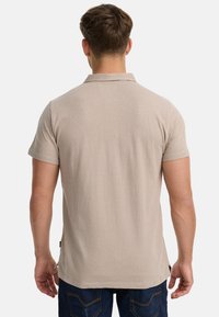 Beige Polohemd mit kurzen Ärmeln aus Baumwolle, klassischem Kragen, schlichtem Design, Rückansicht, mit seitlichen Nähten und leichter Rundung am Saum.