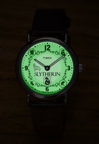 Montre-bracelet Timex lumineuse verte avec l'écusson et les symboles de Serpentard, affichant l'heure 9h10 sur un bracelet en cuir noir.