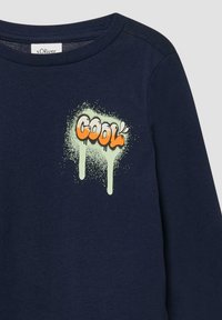Granatowa, długorękawowa koszula z napisem "COOL" w pomarańczowych literach w stylu graffiti oraz wzorem z jasnoniebieskich plam farby na klatce piersiowej.