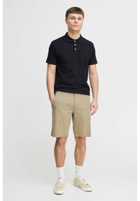 Cămașă polo neagră, pantaloni scurți bej, șosete albe și adidași bej. Cămașa polo are trei butoane și un logo. Pantalonii scurți sunt de lungime până la genunchi și au buzunare.