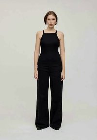 Top preto sem mangas com decote quadrado, combinado com calças pretas de cintura alta e boca de sino. Design simples, textura suave e silhueta ajustada.