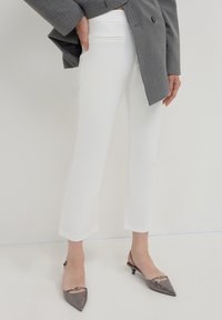 Pantalon tailleur blanc avec une texture lisse, coupe courte, associé à des escarpins gris à talons aiguille brillants et un blazer gris à rayures.