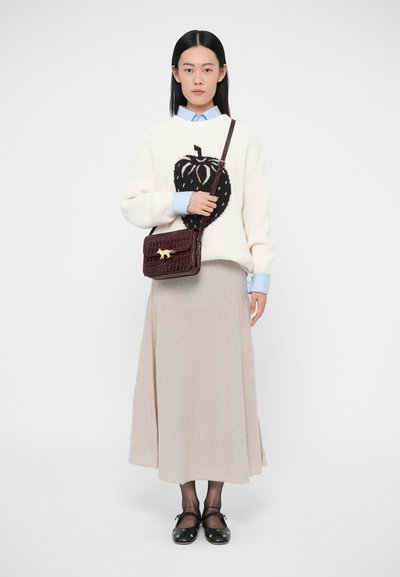 Γυναίκα που φοράει λευκό πουλόβερ με μεγάλο μαύρο γραφικό φράουλας, μπλε πουκάμισο, μπεζ μακριά φούστα, μαύρα μπαλαρίνες, μαύρα καλσόν και μπορντώ τσάντα ώμου.