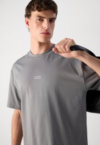 Grå bomulls t-skjorte med rund hals, med en subtil "HUGO"-logo trykt på brystet. Jevn tekstur og regular fit design.