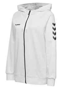 Sweat à capuche blanc zippé, fermeture éclair noire, bandes à chevrons noires sur la manche droite et logo "hummel" sur la poitrine gauche.