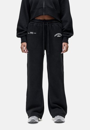 Zwarte katoenen sweatpants met een losse fit, voorzien van een elastische tailleband met trekkoord, en witte bedrukte tekst op de linker heup en rechter dij.