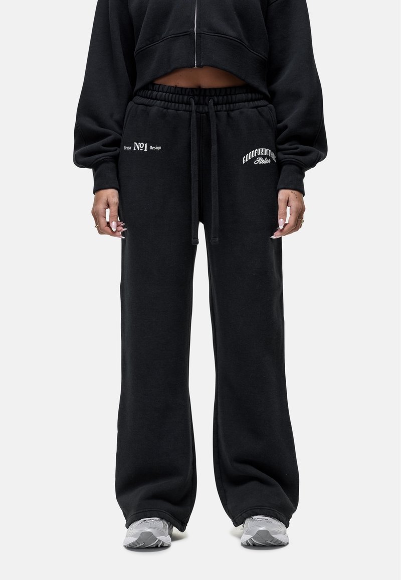 Zwarte katoenen sweatpants met een losse fit, voorzien van een elastische tailleband met trekkoord, en witte bedrukte tekst op de linker heup en rechter dij.