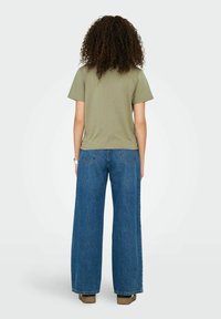 Olivengrøn t-shirt kombineret med vidde jeans i blå denim, med en mellemhøj talje og baglommer. Den glatte stofstruktur er synlig.