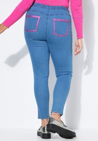 Skinny jeans van lichtblauwe denim met roze achterzakken. Beschikt over een elastische tailleband en roze zijaccenten. Gecombineerd met zilveren schoenen.