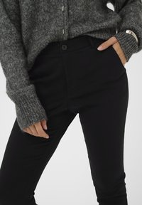 Mustad mustad püksid sileda tekstuuriga, koos hubase halli kudumisega särk, millel on soonikkoes varrukad ja nupuga esiosa.