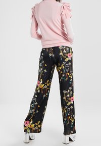 Pull rose avec des épaules volantées associé à un pantalon noir à imprimé floral. Motifs floraux aux couleurs vives sur un fond sombre. Talons épais en argent.