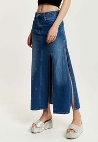 Denim maxi skirt with side slits, a fitted waist, and a smooth texture. Paired with textured silver platform sandals.