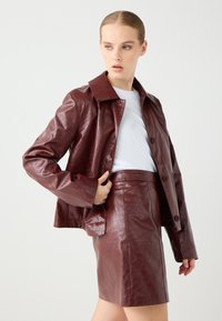 Bordeaux nep-lederen jasje met een kraaghalslijn, voorknopsluiting en een boxy snit, gecombineerd met een bijpassende kokerrok.