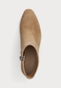 Botte de cheville en suede beige avec un bout pointu, fermeture éclair sur le côté et doublure intérieure lisse. Un accent argenté près de la fermeture éclair est un des éléments caractéristiques.