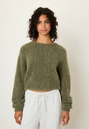 Olijfgroene cropped trui van pluizig, gestructureerd materiaal met lange mouwen en een wijde halslijn, gecombineerd met grijze joggingbroek.