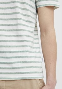 Stribet kortærmet t-shirt i off-white og lysegrøn. Lavet af blødt stof, med vandrette striber og et lille mærketikette ved kanten.