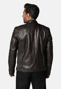 Veste de moto en cuir brun avec un design de épaules matelassées, des panneaux latéraux côtelés et des accents zippés sur les manches.