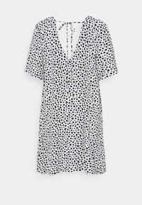 Vestido de manga corta en blanco con estampado de corazones negros, con un escote en V profundo y cierre de lazo en la parte posterior. Tejido suave, corte holgado.