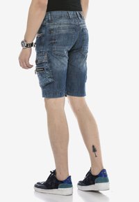Cargo-Shorts aus Jeans in verwaschenem Blau mit mehreren Taschen, Reißverschlussdetails und einer lockeren Passform. Tragen Sie dazu schwarze Sneakers mit blauen Akzenten.